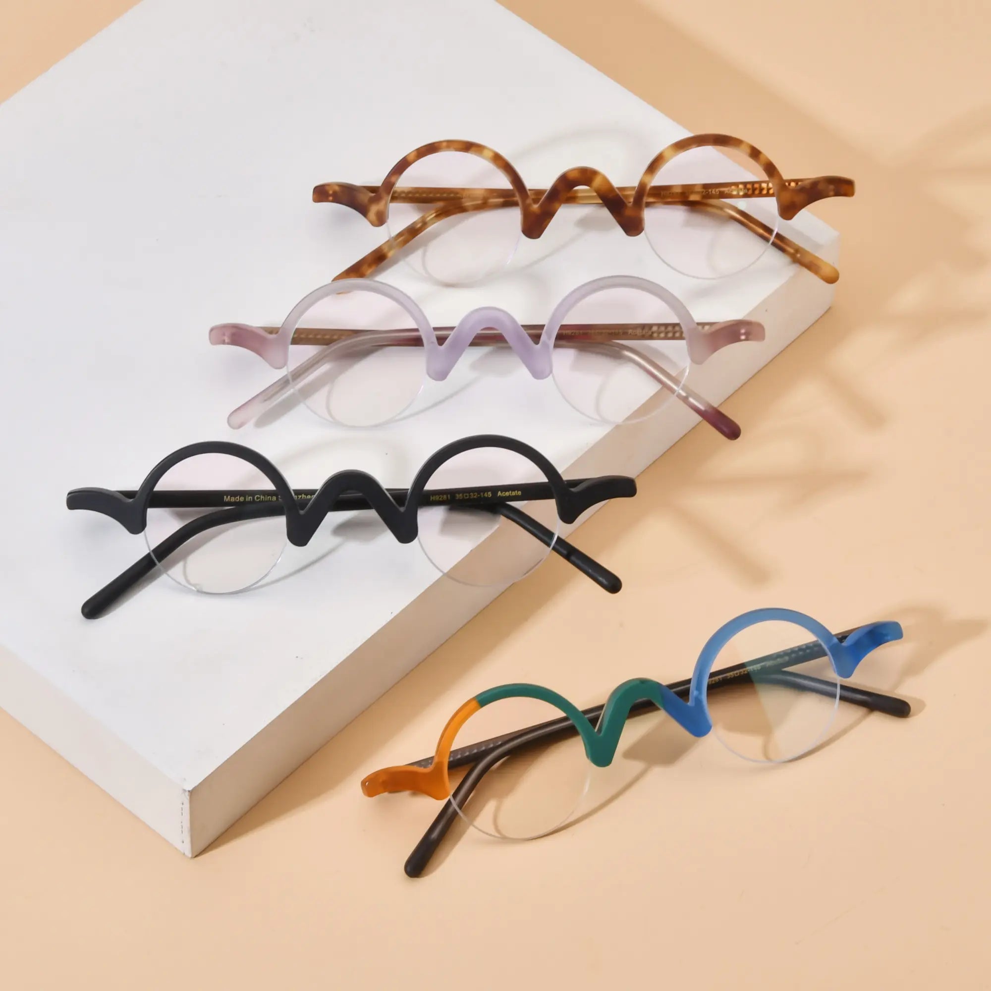 Group display of VoyueLens™ semi-rimless browline eyeglasses featuring Tortoiseshell, Lilac-Rose, Solid Black, and Teal-Blue color variants on beige background, highlighting wave top design and matte acetate frames.